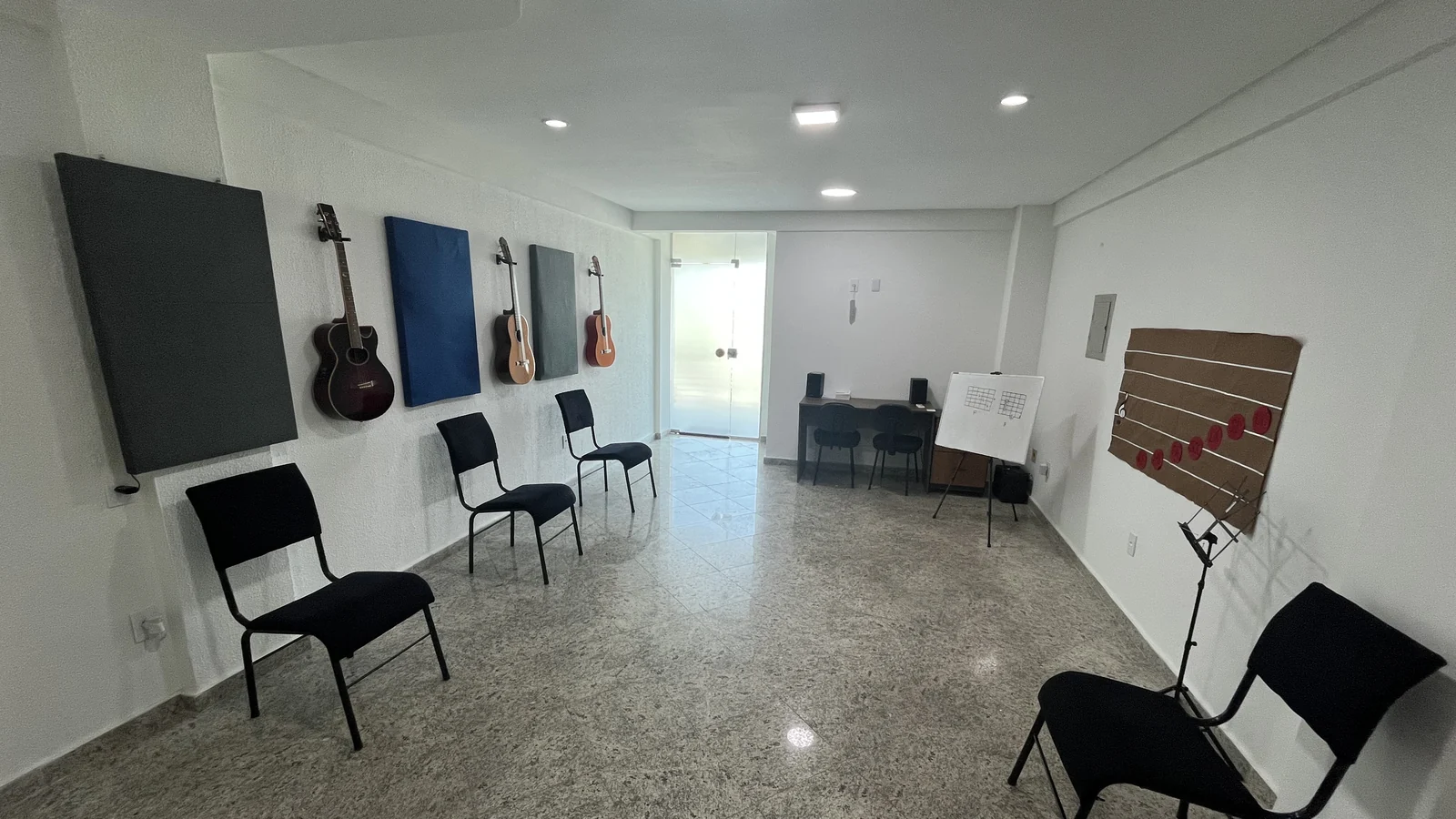 Sala de aula da Tocante Centro Musical em Manaus, com violões na parede, tratamento acústico e cadeiras para aula em grupo